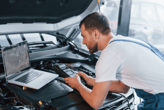 Young man in white shirt and blue uniform repairs automobile Young man in white shirt and blue uniform repairs automobile